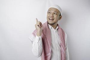 Excited Asian Muslim man pointing at the copy space beside him, isolated by white background photo