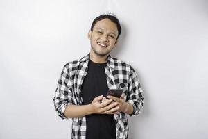 A portrait of a happy Asian man is smiling while holding on his phone, isolated by white background photo