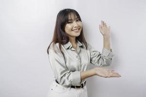 Excited Asian woman wearing sage green shirt pointing at the copy space beside her, isolated by white background photo