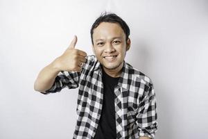 Excited Asian man wearing tartan shirt gives thumbs up hand gesture of approval, isolated by white background photo
