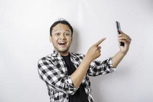 A portrait of a happy Asian man is smiling while holding on his phone, isolated by white background photo