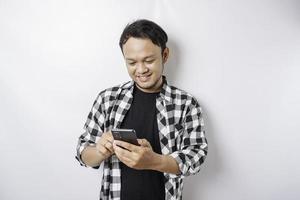 un retrato de un hombre asiático feliz sonríe mientras sostiene su teléfono, aislado por fondo blanco foto