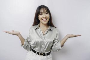 Excited Asian woman wearing sage green shirt pointing at the copy space beside her, isolated by white background photo