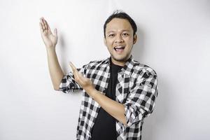 Smiling Asian man wearing tartan shirt is pointing at the copy space on top of him, isolated by white background photo