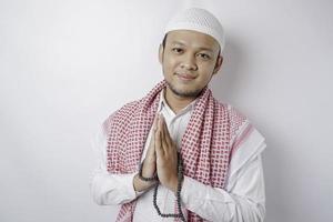 Smiling young Asian Muslim man, gesturing traditional greeting isolated over white background photo