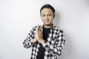 Smiling young Asian man wearing tartan shirt, gesturing traditional greeting isolated over white background photo