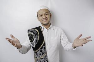 A portrait of a happy Asian Muslim man with prayer rug on his shoulder is smiling isolated by white background photo