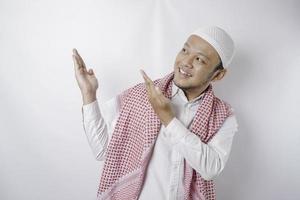 Excited Asian Muslim man pointing at the copy space beside him, isolated by white background photo