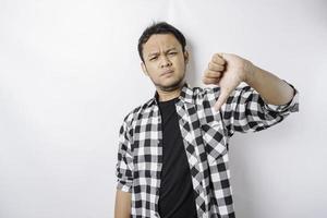 Disappointed Asian man wearing tartan short gives thumbs down hand gesture of approval, isolated by white background photo