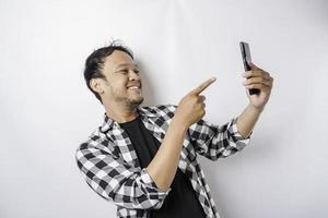 un retrato de un hombre asiático feliz sonríe mientras sostiene su teléfono, aislado por fondo blanco foto