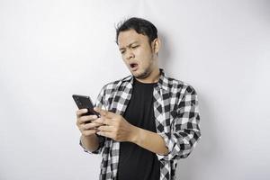 A dissatisfied young Asian man looks disgruntled wearing tartan shirt irritated face expressions holding his phone photo