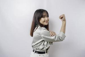 Excited Asian woman wearing a sage green shirt showing strong gesture by lifting her arms and muscles smiling proudly photo