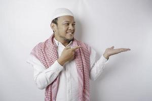 Excited Asian Muslim man pointing at the copy space beside him, isolated by white background photo