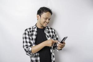 A portrait of a happy Asian man is smiling while holding on his phone, isolated by white background photo