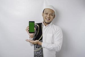 A portrait of a happy Asian Muslim man smiling while showing copy space on his phone, isolated by white background photo