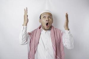 Shocked Asian Muslim man pointing at the copy space on top of him, isolated by a white background photo