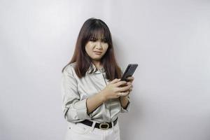 A dissatisfied young Asian woman looks disgruntled wearing sage green shirt irritated face expressions holding her phone photo