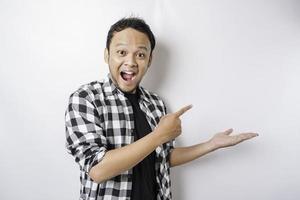 Shocked Asian man wearing tartan shirt is pointing at the copy space beside him, isolated by white background photo