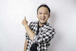 Smiling Asian man wearing tartan shirt is pointing at the copy space on top of him, isolated by white background photo