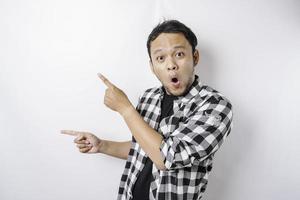 Shocked Asian man wearing tartan shirt is pointing at the copy space beside him, isolated by white background photo