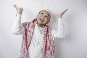 Smiling Asian Muslim man pointing at the copy space on top of him, isolated by white background photo