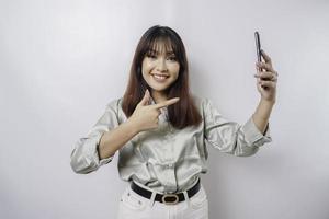 A portrait of a happy Asian woman wearing a sage green shirt and holding her phone, isolated by white background photo