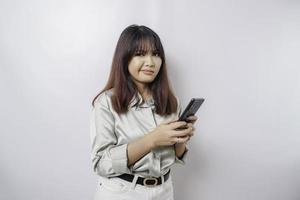 A dissatisfied young Asian woman looks disgruntled wearing sage green shirt irritated face expressions holding her phone photo