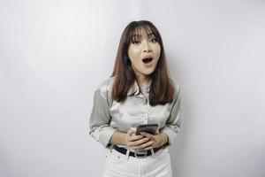 Shocked Asian woman wearing sage green shirt and holding her phone, isolated by white background photo