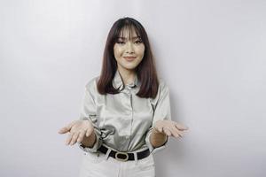joven asiática con pantalones verde salvia que presenta una idea mientras mira sonriendo en un fondo blanco aislado foto