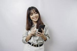 A portrait of a happy Asian woman wearing a sage green shirt and holding her phone, isolated by white background photo