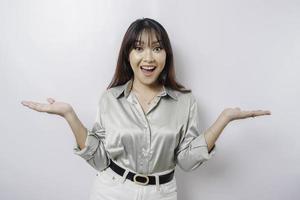 Excited Asian woman wearing sage green shirt pointing at the copy space beside her, isolated by white background photo