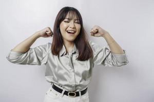 Excited Asian woman wearing a sage green shirt showing strong gesture by lifting her arms and muscles smiling proudly photo