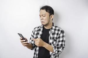 A dissatisfied young Asian man looks disgruntled wearing tartan shirt irritated face expressions holding his phone photo