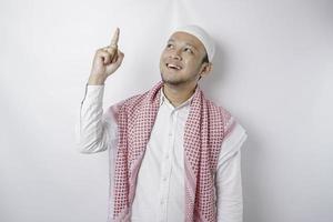 Smiling Asian Muslim man pointing at the copy space on top of him, isolated by white background photo