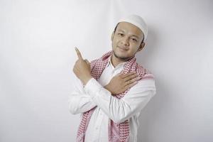 Smiling Asian Muslim man pointing at the copy space on top of him, isolated by white background photo