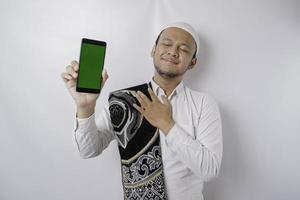 Portrait of a peaceful Asian Muslim man is showing copy space on his phone and smiling feel relief photo