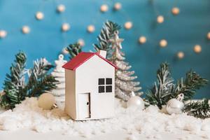 Abstract Advent Christmas Background. Toy model house and winter decorations ornaments on blue background with snow. Christmas with family at home concept. photo