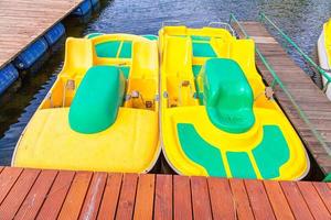 Pedal boats or paddle boats catamarans station. Yellow water bicycles locked at lake marina dock pier on sunny summer day. Summer leisure activity outdoors. photo