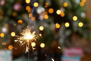 Christmas glittering sparklers candle burns in Christmas tree background. Xmas lighting decoration at home indoor. Festive Magic sparks lights for holiday party. Christmas eve with fireworks. photo