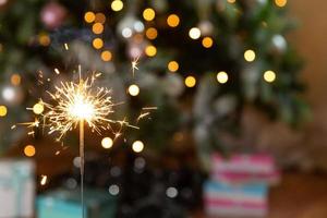 velas de bengalas brillantes de navidad se queman en el fondo del árbol de navidad. decoración de iluminación navideña en el interior de la casa. luces de chispas mágicas festivas para fiestas navideñas. Nochebuena con fuegos artificiales. foto
