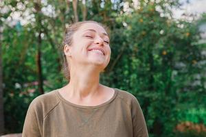 mujer joven sonriendo al aire libre. hermosa chica brunete descansando sobre un fondo verde de parque o jardín. mujer feliz libre en verano. libertad felicidad despreocupada gente feliz concepto. foto