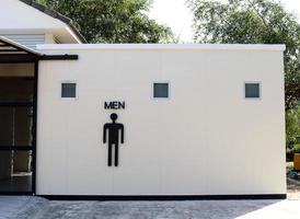 Black color of man sign on toilet's white wall building in natural environment. photo