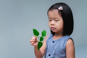 una linda niña asiática está mirando una pequeña copa de árbol en su mano. el retoño del árbol está en manos del niño semillas de plantas vivas. dia del arbol día nacional de la tierra. espacio vacío para texto. foto