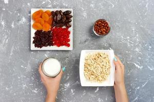 The girl took milk to pour it into oatmeal. Useful and healthy breakfast on a gray background, top view photo