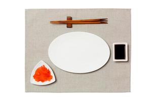 Empty oval white plate with chopsticks for sushi, ginger and soy sauce on grey napkin background. Top view with copy space for you design photo