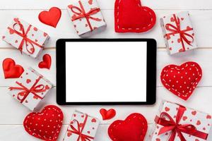 pantalla en blanco de tableta digital con caja de regalo y decoración de corazones en mesa de madera. vista superior. fondo del concepto del día de san valentín foto