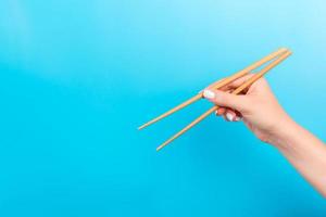 Female hand with chopsticks on blue background. Traditional asian food with emty space for your design photo