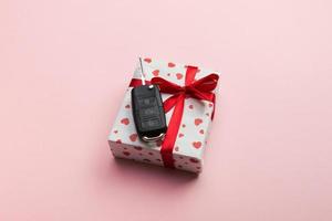 Give gift car key concept top view. Present box with red ribbon bow, heart and car key on coral colored background photo