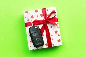 Give gift car key concept top view. Present box with red ribbon bow, heart and car key on green colored background photo