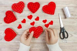 Valentine day theme. Workplace for preparing handmade decorations. Top view of female hands sew felt heart. Packed gifts, tools shabby wooden table photo